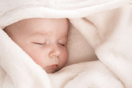 Baby sleeping covered with soft white blanketの写真素材