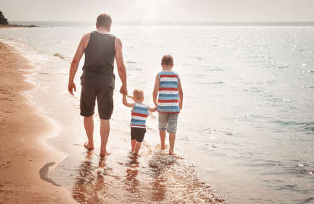 Father and sons walking at the beach at seaの写真素材