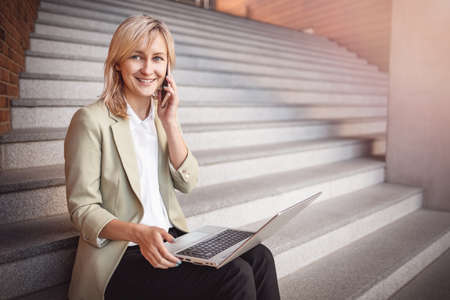 happy young woman with laptop and smartphone sitting on the stairsの写真素材