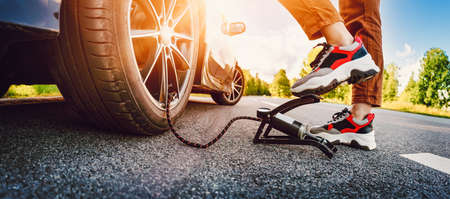 Driver using a foot pump to inflate a tire. Woman near car wheel outdoorsの写真素材