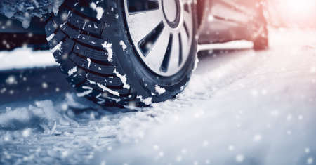 Closeup of the car tire on winter road covered with snow in snowfall in sunny dayの写真素材