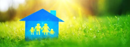 Blue family house is on green grass on a sunny day. Model of a housing with a shape of the family of two parents and two children.の写真素材