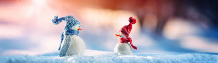 Little knitted snowmen on soft snow on blue background. Christmas conceptual symbol.