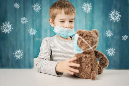 Little boy sitting at the table with a teddy bear in medical facial masksの写真素材