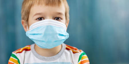 Boy in medical face protection mask indoors on blue background.