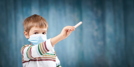 Boy in medical face protection mask indoors on blue background.の写真素材