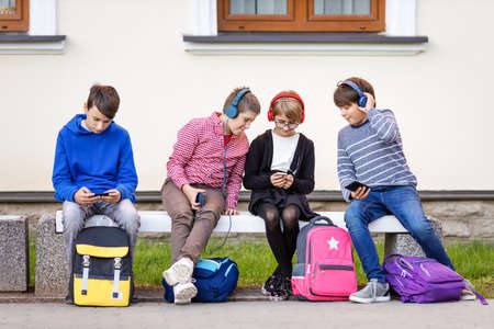 Children with rucksacks sitting on the bench in the park near the schoolの写真素材