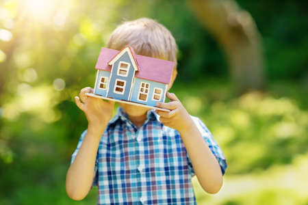 Little child holding in his hands model of the blue wooden house. Concept of the selling, buying and renting of the house.の写真素材
