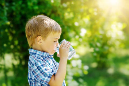 Cute boy drinking a glass of pure water in nature. Concept of the provision of clean, mineral aqua in the world.の写真素材