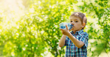 Cute boy drinking a bottle of pure water in nature. Concept of the provision of clean, mineral aqua in the world.の写真素材