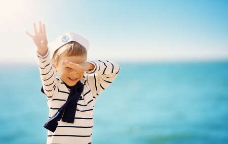 Cute boy in sailor cap standing on the seashore of the seaの写真素材