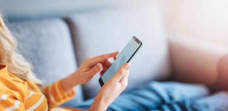 Young woman on the couch using her smartphone.の写真素材