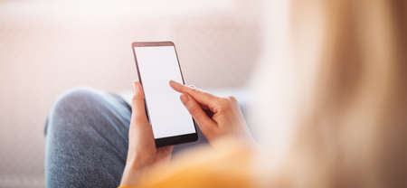 Young woman on the couch using her smartphone.の写真素材