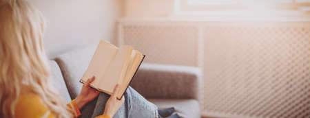 Young woman on the couch reading an interesting book.の写真素材