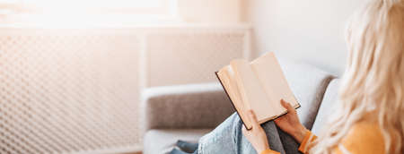 Young woman on the couch reading an interesting book.の写真素材
