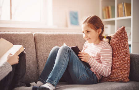 Pretty girl have a rest on the cozy couch with interesting bookの写真素材