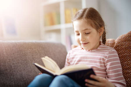 Pretty girl have a rest on the cozy couch with interesting bookの写真素材