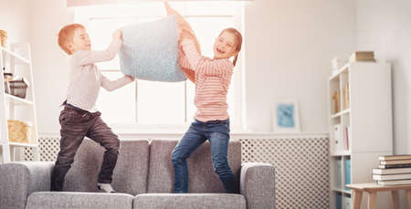 Cute children fighting by pillows on the sofaの写真素材
