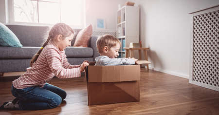 Cute children playing with cardboard box in living room.の写真素材