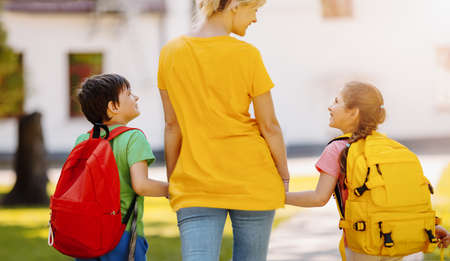 Mother walking with son and daughter on the schoolyard. Mom accompanies children to the school. Concept of family relationships and studying.の写真素材