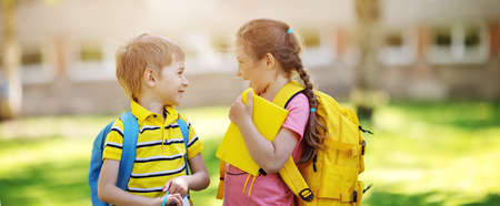 Two cute children standing in the schoolyard park. Concept of the communication between pupils and...