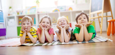 Group of children lying on the floor and looking in the camera.