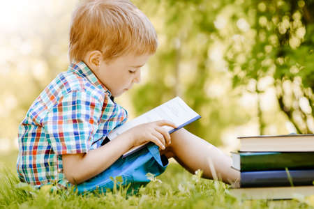 Little boy sitting on the meadow and reading a book.の写真素材
