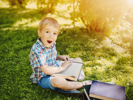 Little boy sitting on the meadow and reading a book.の写真素材