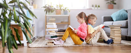 Two children sitting on the floor in the room and reading booksの写真素材