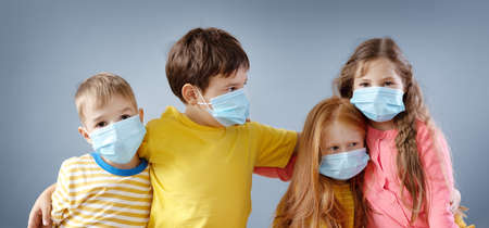 Group of four children in medical mask standing indoor.の写真素材