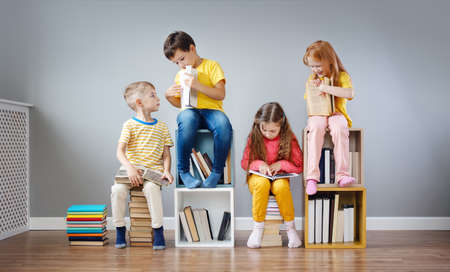 Group of children sitting on the books stacks and on the bookshelves in the room and reading periodical.の写真素材