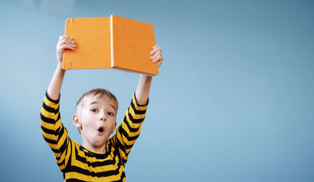 Surprised boy holding in his hands an interesting bookの写真素材
