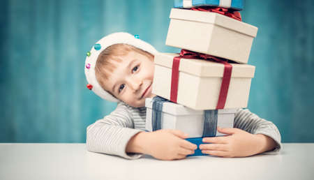 Cute child sitting at the table with stack of giftboxesの写真素材