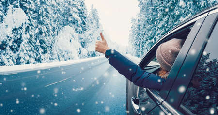 Happy woman in the car gesture finger up on the snowy background.の写真素材