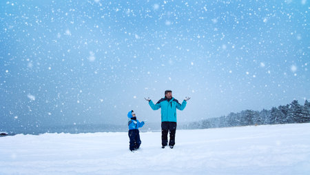 Father and his son standing on the snowfall in the snowy winter forestの写真素材