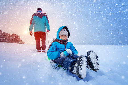 Father pulling sled with his lovely smiling son in snowfallの写真素材