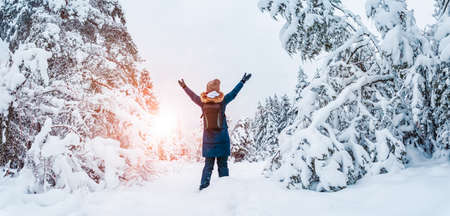 Happy woman with hands up standing in the snowy forest in snowfall.の写真素材