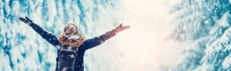 Happy woman with hands up standing in the snowy forest in snowfall.の写真素材