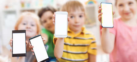 Group of children holding in their hands smartphones with mock-up screen indoorsの写真素材