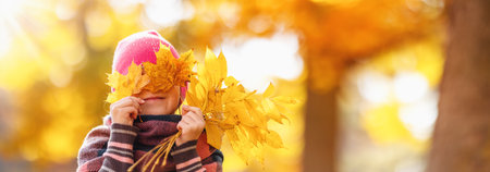 Happy child hiding his eyes behind the maple leaves.の写真素材