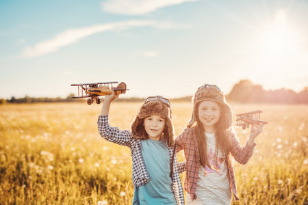 Boy and girl plaing with wooden planes on the field in sunsetの写真素材