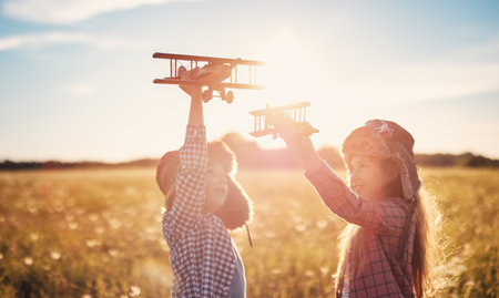Boy and girl plaing with wooden planes on the field in sunsetの写真素材