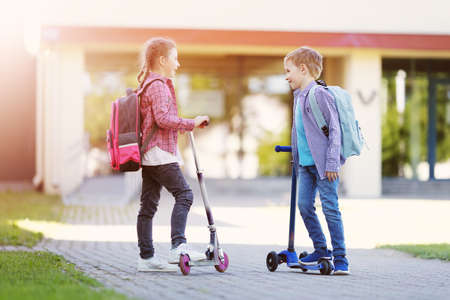 Girl and boy standing with scooters at school and talking together.の写真素材
