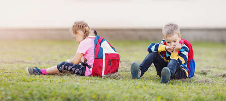 A boy and a girl quarreling and are sitting on the grass in the schoolyard back to backの写真素材