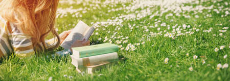 Young woman lying on the field and reading some booksの写真素材