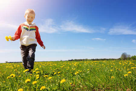 Cute child running outdoors in nature with bunch of dandelionsの写真素材
