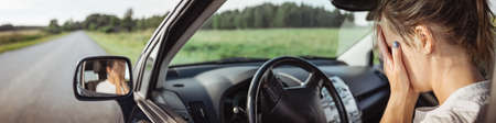 Upset woman sitting in the car and covering face with her handsの写真素材