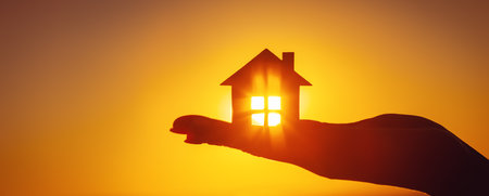 Womans hand holding a model of a house on sunset eveningの写真素材