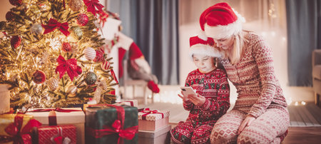 Mother and daughter sitting with smartphone on the floor indoors in Christmas eve.の写真素材
