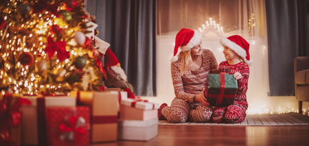 Mother and daughter sitting on the floor indoors and giving present box each other in Christmas eve.の写真素材